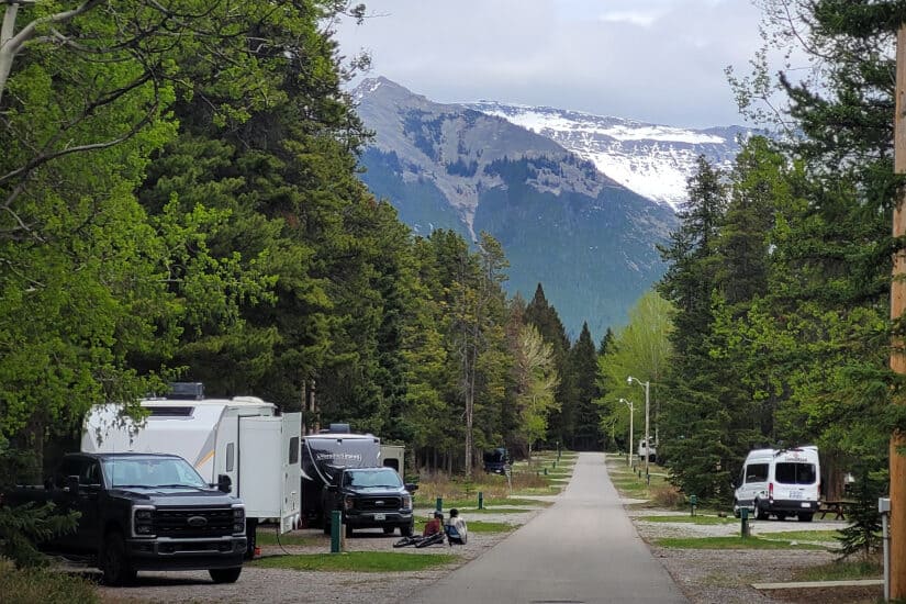 Un emplacement du Trailer Court, à Tunnel Mountain : des VR branchés le long d’une allée pavée bordée d’arbres, bornes de services visibles